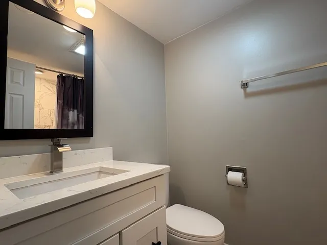 a bathroom with a granite countertop sink vanity mirror and toilet