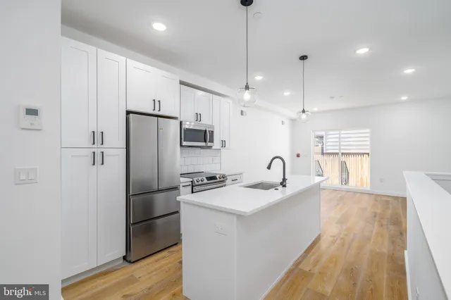 a kitchen with stainless steel appliances granite countertop a refrigerator a sink a stove and a wooden floors