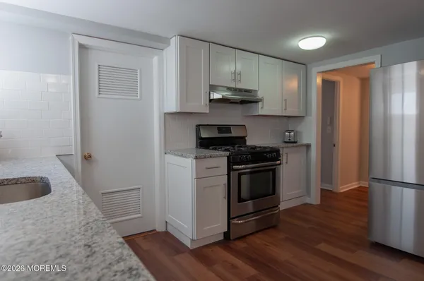 a kitchen with stainless steel appliances granite countertop a stove a refrigerator and a sink with wooden floors