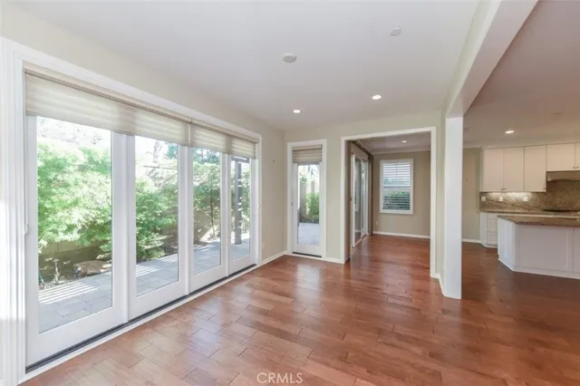 a view of an empty room with wooden floor and a kitchen