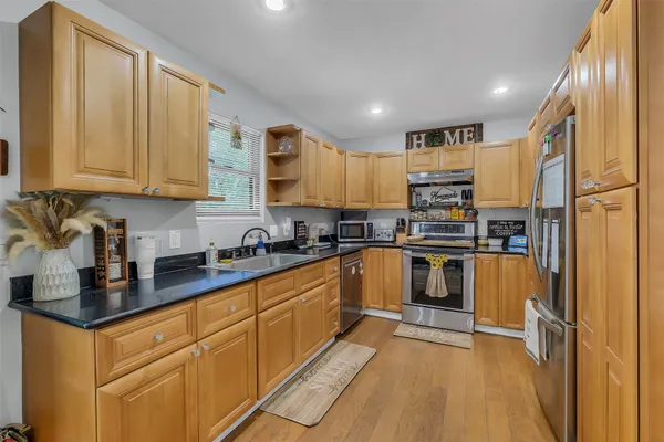 a kitchen with stainless steel appliances granite countertop a refrigerator a sink dishwasher a stove with wooden cabinets and floor