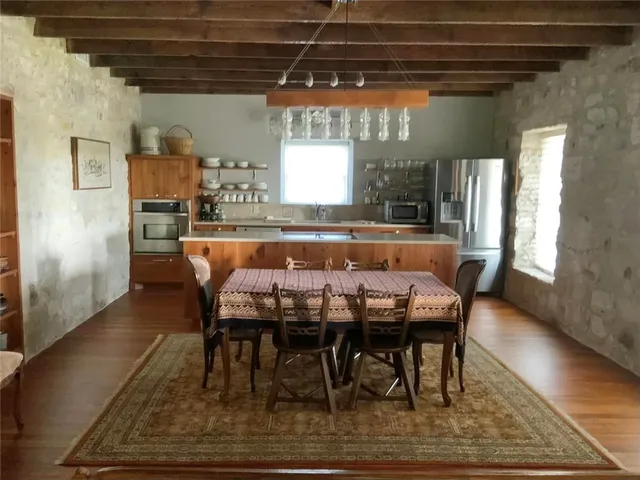 a dining hall with stainless steel appliances granite countertop a table chairs and a wooden floor