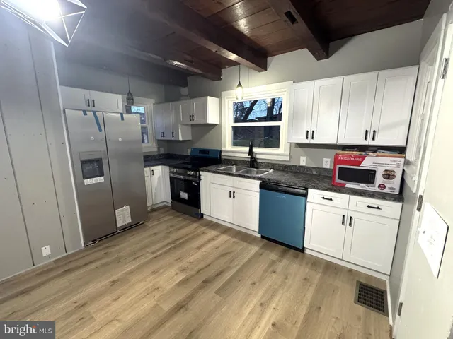 a kitchen with stainless steel appliances granite countertop a stove a sink dishwasher a refrigerator and white cabinets with wooden floor