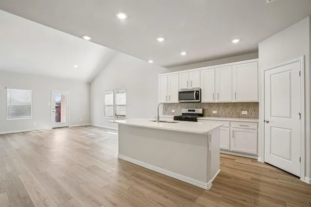 a kitchen with stainless steel appliances granite countertop a stove top oven a sink dishwasher and a refrigerator with wooden floor