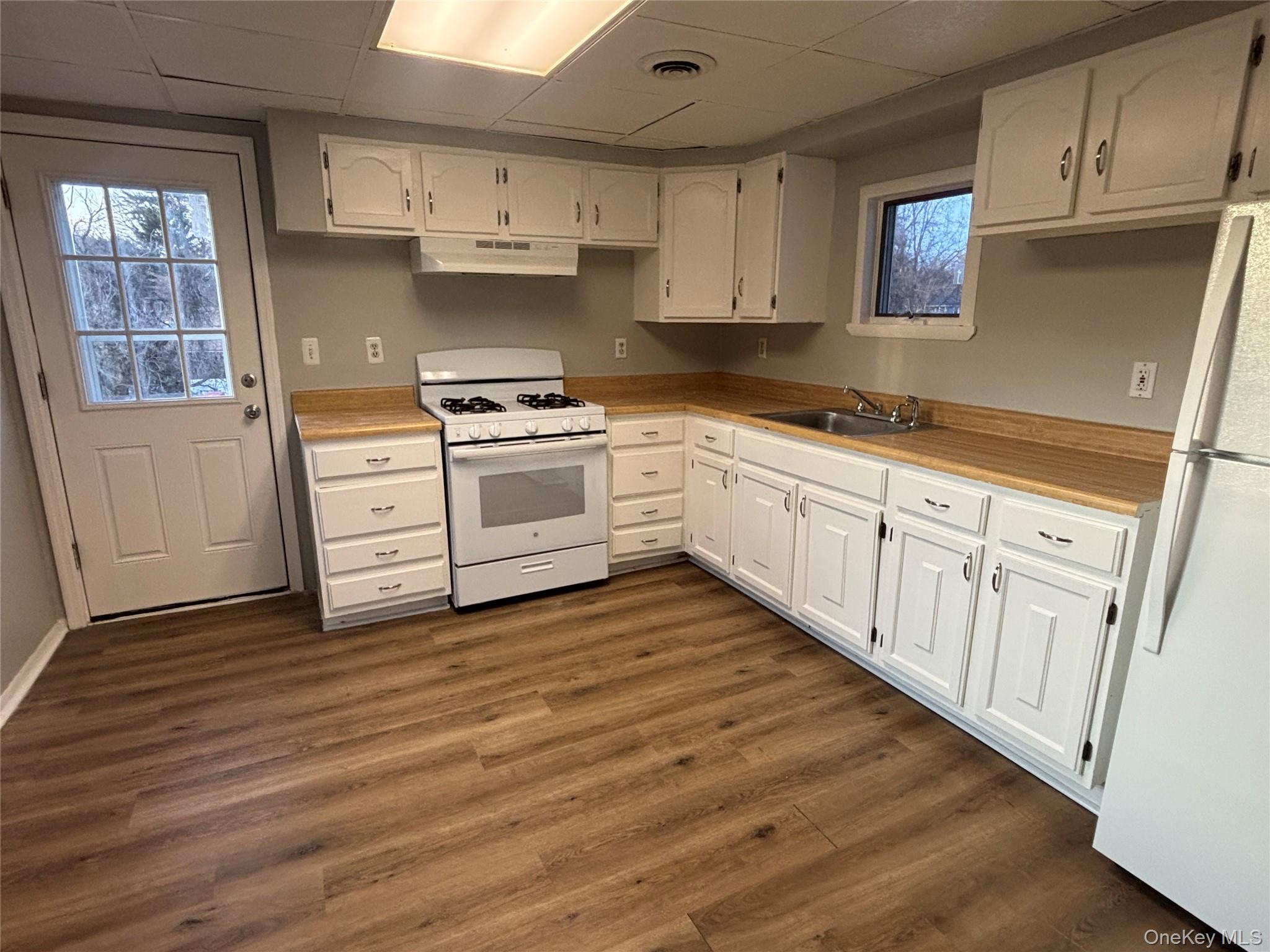 114 Sprague Avenue, Unit 2 Middletown, NY 10940 - Photo 5 of 13 Kitchen featuring white appliances, light countertops, a paneled ceiling, white cabinetry, and dark wood finished floors