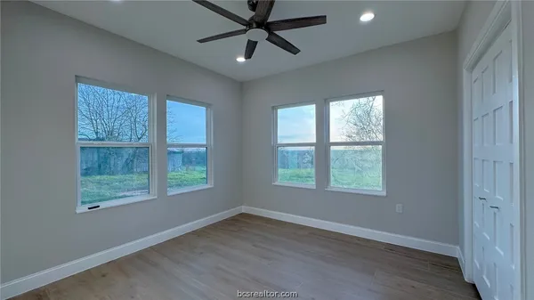 an empty room with wooden floor ceiling fan and windows