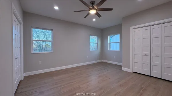 an empty room with wooden floor closet and windows
