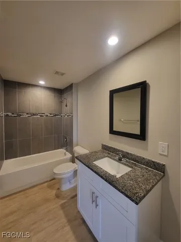 a bathroom with a granite countertop sink a toilet a mirror and bathtub