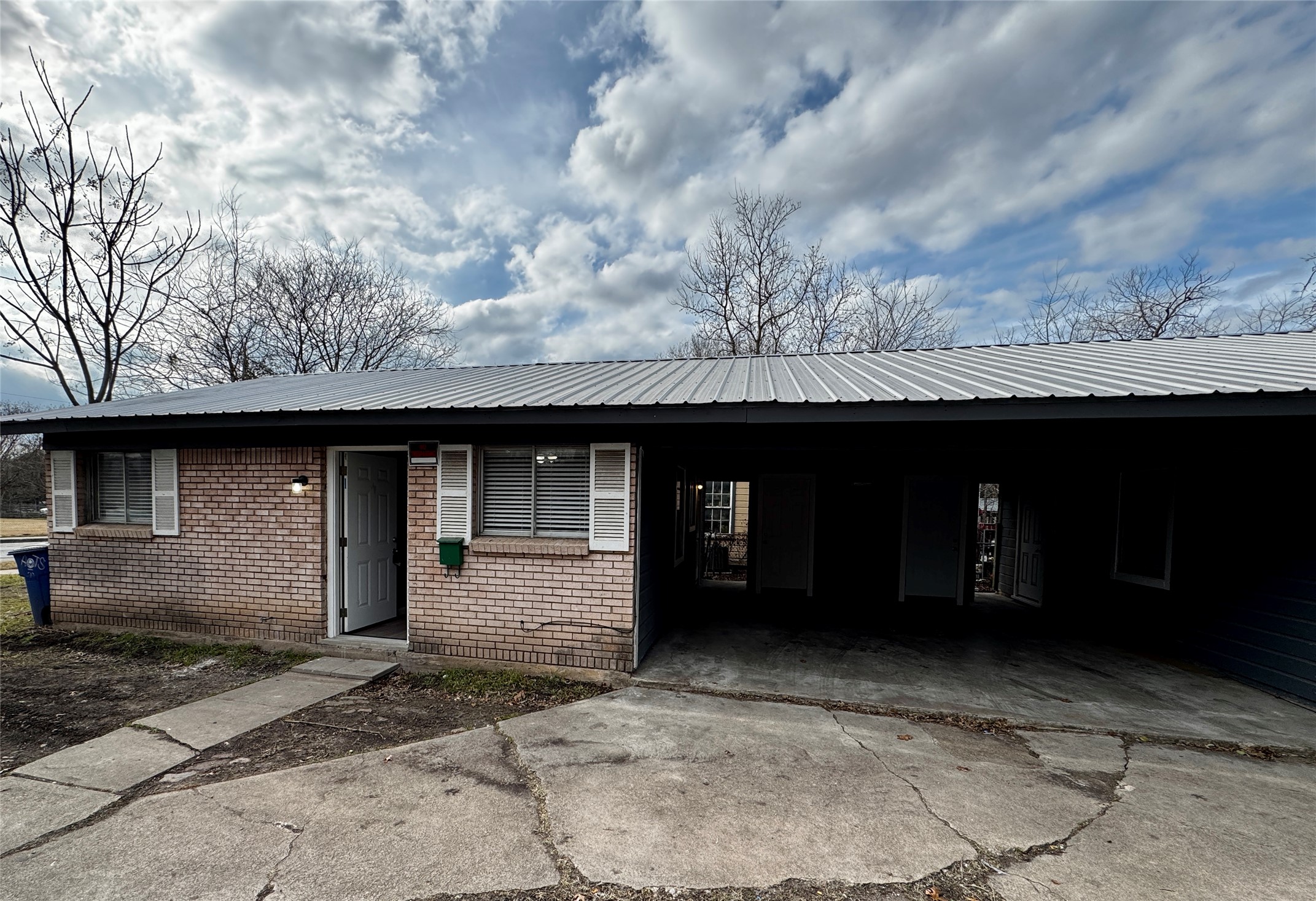 View of front of home with brick siding, an attached carport, a metal roof, and concrete driveway