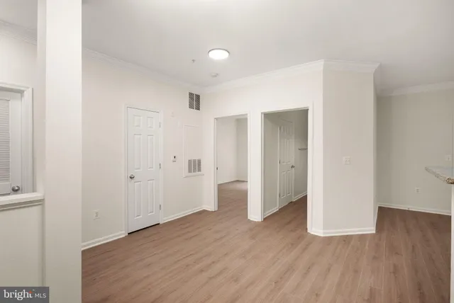 an empty room with wooden floor and a kitchen