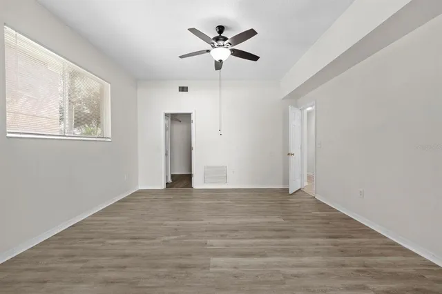 a view of an empty room with wooden floor and a ceiling fan