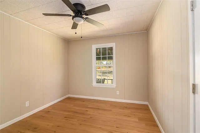 an empty room with wooden floor ceiling fan and windows