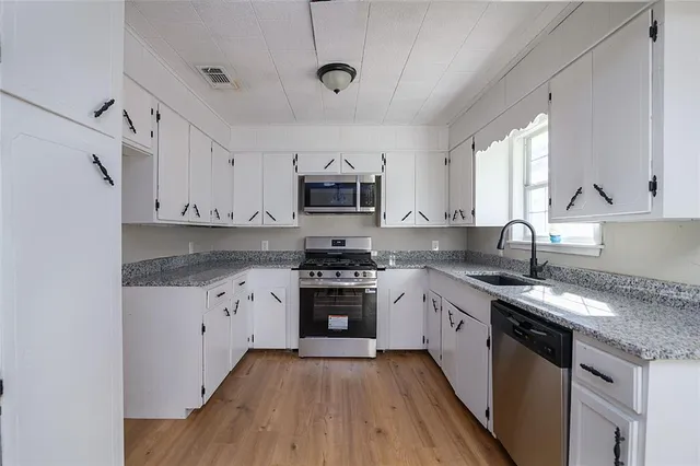 a kitchen with granite countertop a sink stainless steel appliances and white cabinets