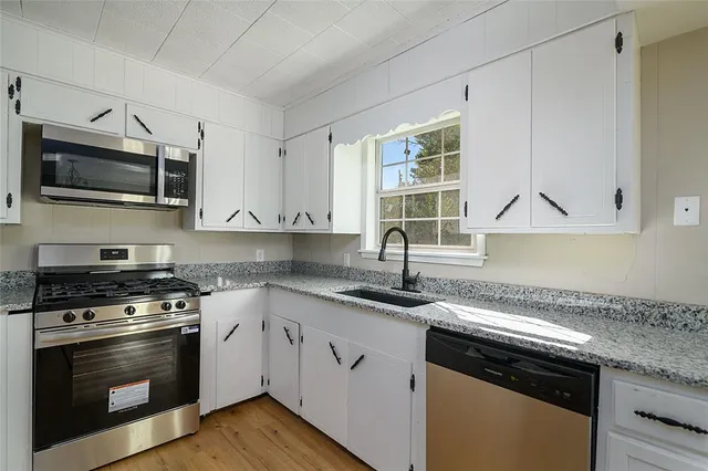 a kitchen with granite countertop a sink dishwasher stove and microwave with wooden floor
