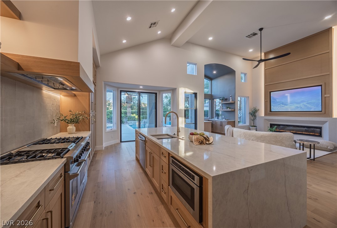 8800 Lusso Las Vegas, NV 89134 - Photo 85 of 85 Kitchen featuring stainless steel appliances, light stone counters, light wood-style flooring, open floor plan, and a glass covered fireplace