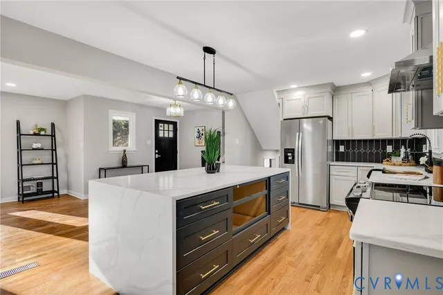 a kitchen with stainless steel appliances kitchen island granite countertop a refrigerator a stove a sink dishwasher and white cabinets with wooden floor
