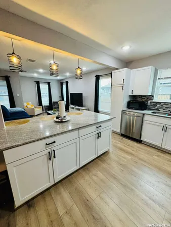 a kitchen with stainless steel appliances granite countertop a sink dishwasher stove and white cabinets with wooden floor