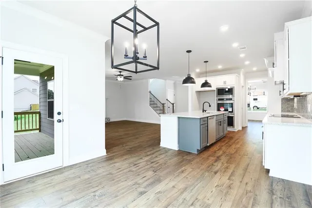 a kitchen with stainless steel appliances kitchen island wooden floors cabinets and living room view