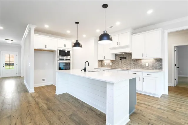 a kitchen with stainless steel appliances granite countertop a sink a stove a refrigerator and white cabinets with wooden floor