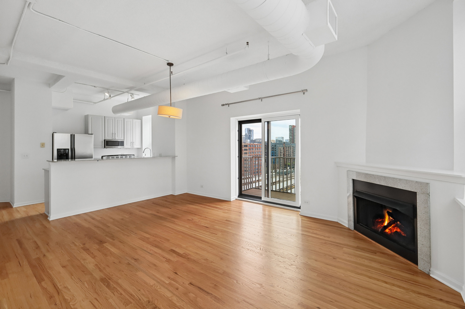 161 West Harrison Street, Unit 1007 Chicago, IL 60605 - Photo 4 of 35 a view of a kitchen and an empty room with wooden floor and a fireplace