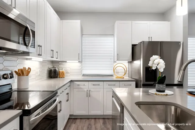 a kitchen with granite countertop a sink white cabinets and stainless steel appliances