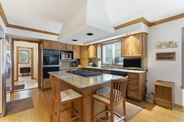 a kitchen with stainless steel appliances granite countertop a stove top oven a sink a dining table and chairs with wooden floor