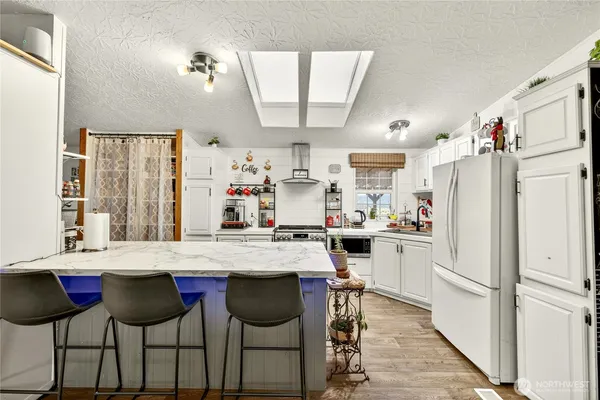 a kitchen with stainless steel appliances granite countertop a refrigerator a sink dishwasher a dining table and chairs with wooden floor