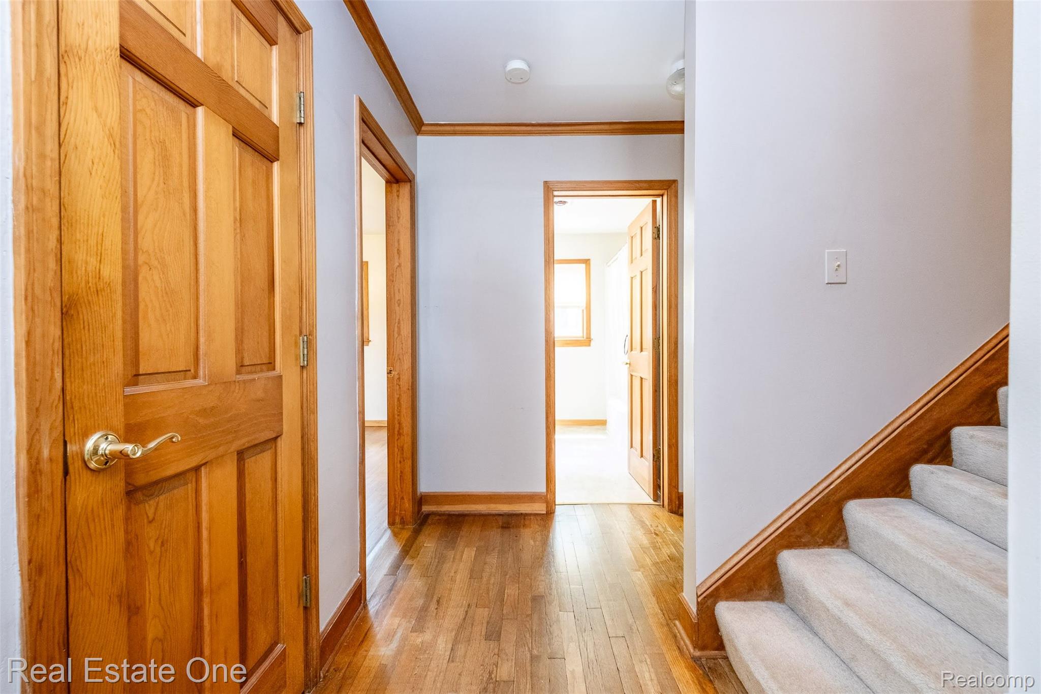 11030 Marshall Road South Lyon, MI 48178 - Photo 36 of 83 Bright hallway featuring warm wood-finish flooring, classic six-panel wood doors with brass hardware, and a staircase with white-painted treads and wood railings