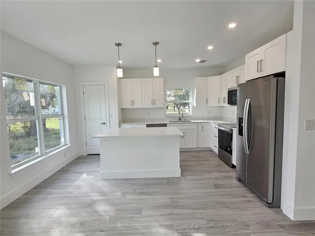 a large kitchen with kitchen island a stove a refrigerator a sink dishwasher and a fireplace with wooden floor