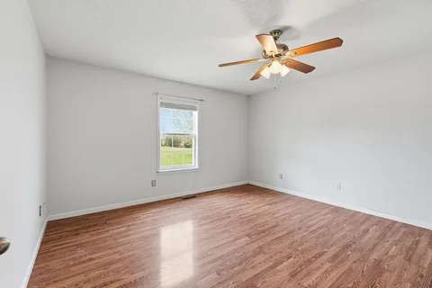 an empty room with wooden floor fan and windows