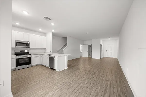 a kitchen with stainless steel appliances a stove top oven a sink dishwasher and a refrigerator with wooden floor