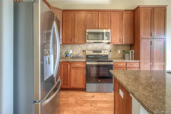 a kitchen with stainless steel appliances granite countertop a refrigerator a stove and a sink with wooden cabinets