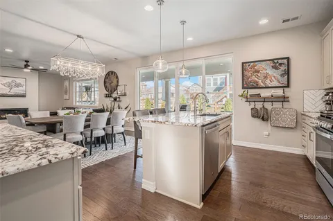 a room with stainless steel appliances kitchen island granite countertop a stove a sink a refrigerator and a dining table with wooden floor