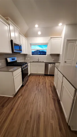a white kitchen with wooden floors and stainless steel appliances