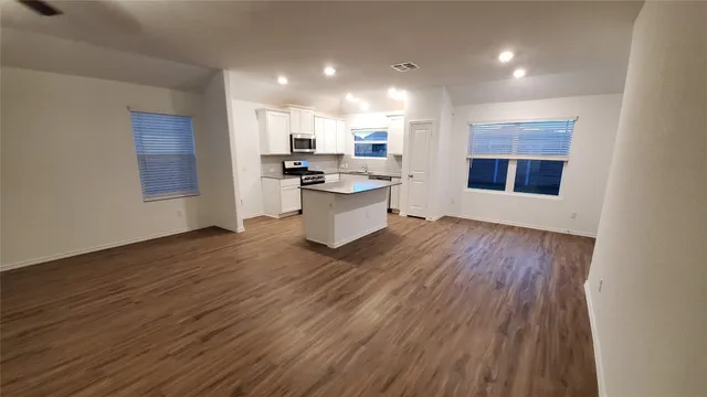 a large white kitchen with kitchen island a sink wooden floor and a large window