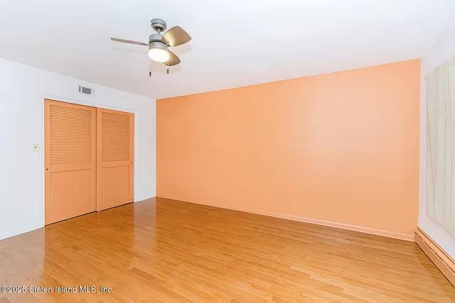 a view of an empty room with wooden floor and a ceiling fan