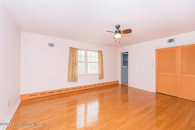 an empty room with wooden floor chandelier fan and windows