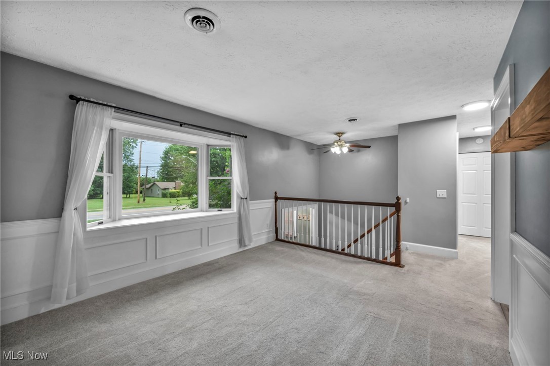 47655 Cooper Foster Park Road Amherst, OH 44001 - Photo 6 of 49 Empty room with a decorative wall, wainscoting, carpet floors, a textured ceiling, and a ceiling fan