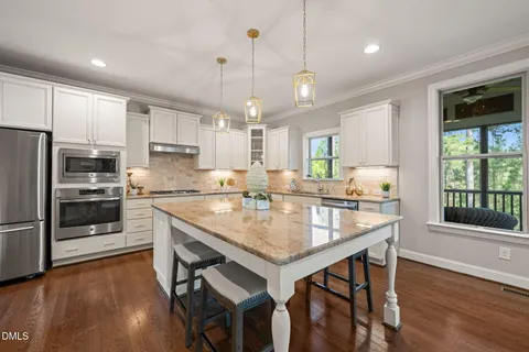 a kitchen with stainless steel appliances granite countertop a stove a refrigerator a sink dishwasher a dining table and chairs with wooden floor