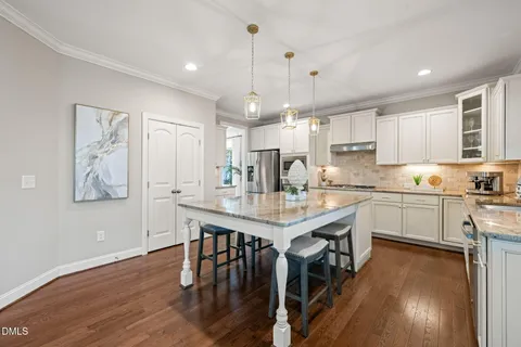 a kitchen with stainless steel appliances granite countertop a stove a refrigerator a kitchen island a sink and white cabinets with wooden floor