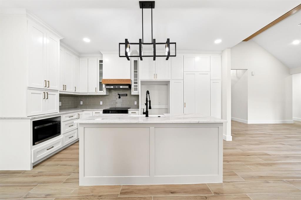 120 Springwood Road Enchanted Oaks, TX 75156 - Photo 15 of 37 Modern kitchen featuring white cabinetry, a center island with a stone countertop, a built-in microwave, and wood-finish flooring