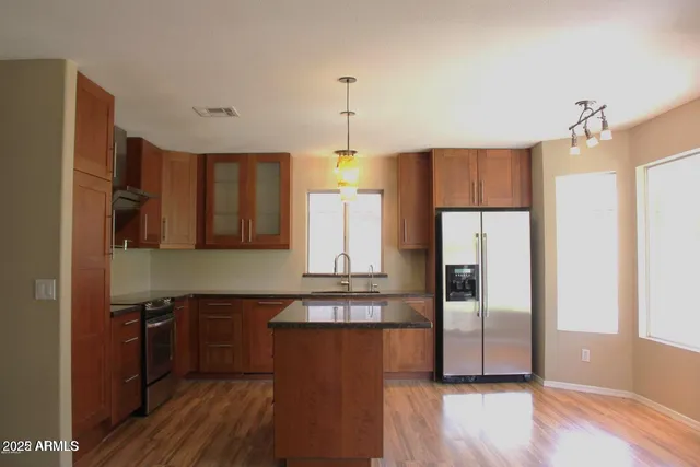 a kitchen with stainless steel appliances granite countertop a refrigerator a sink dishwasher a stove and a dining table with wooden floor