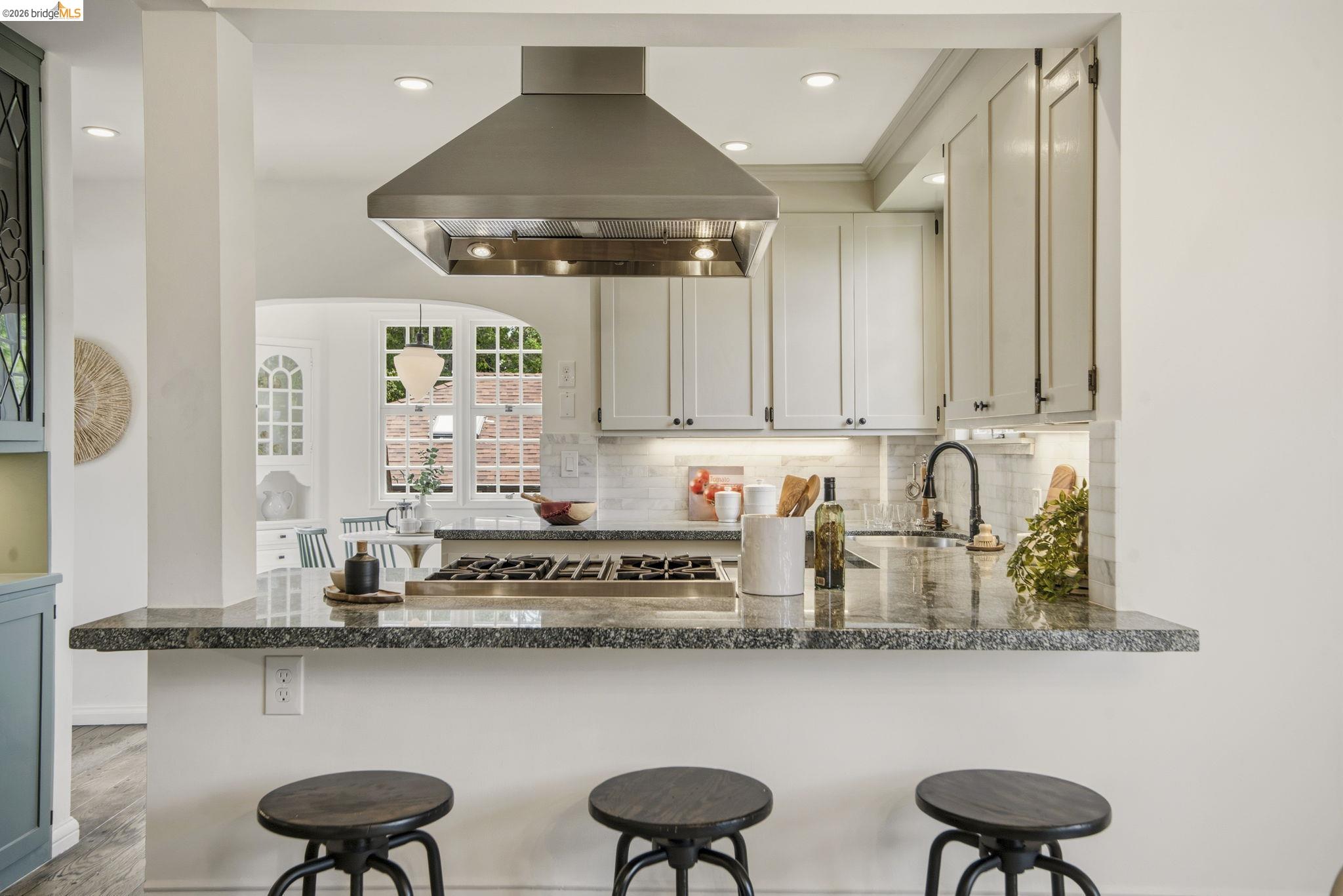 1087 Hubert Road Oakland, CA 94610 - Photo 11 of 67 Open-concept kitchen featuring a built-in cooktop, stainless steel range hood, white cabinetry, dark stone countertops, and a subway tile backsplash