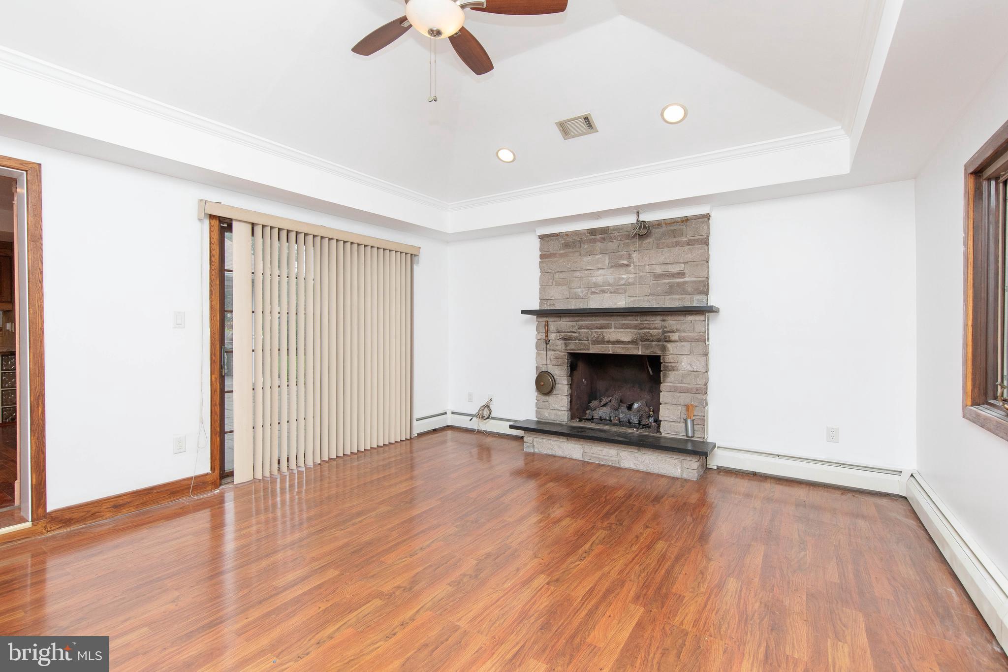 95 Radburn Road Huntingdon Valley, PA 19006 - Photo 10 of 40 an empty room with wooden floor a ceiling fan a fireplace and entryway