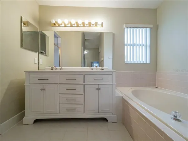 a spacious bathroom with a double vanity sink a mirror a bathtub and window