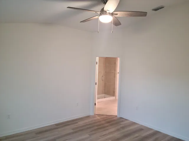 an empty room with wooden floor fan and windows