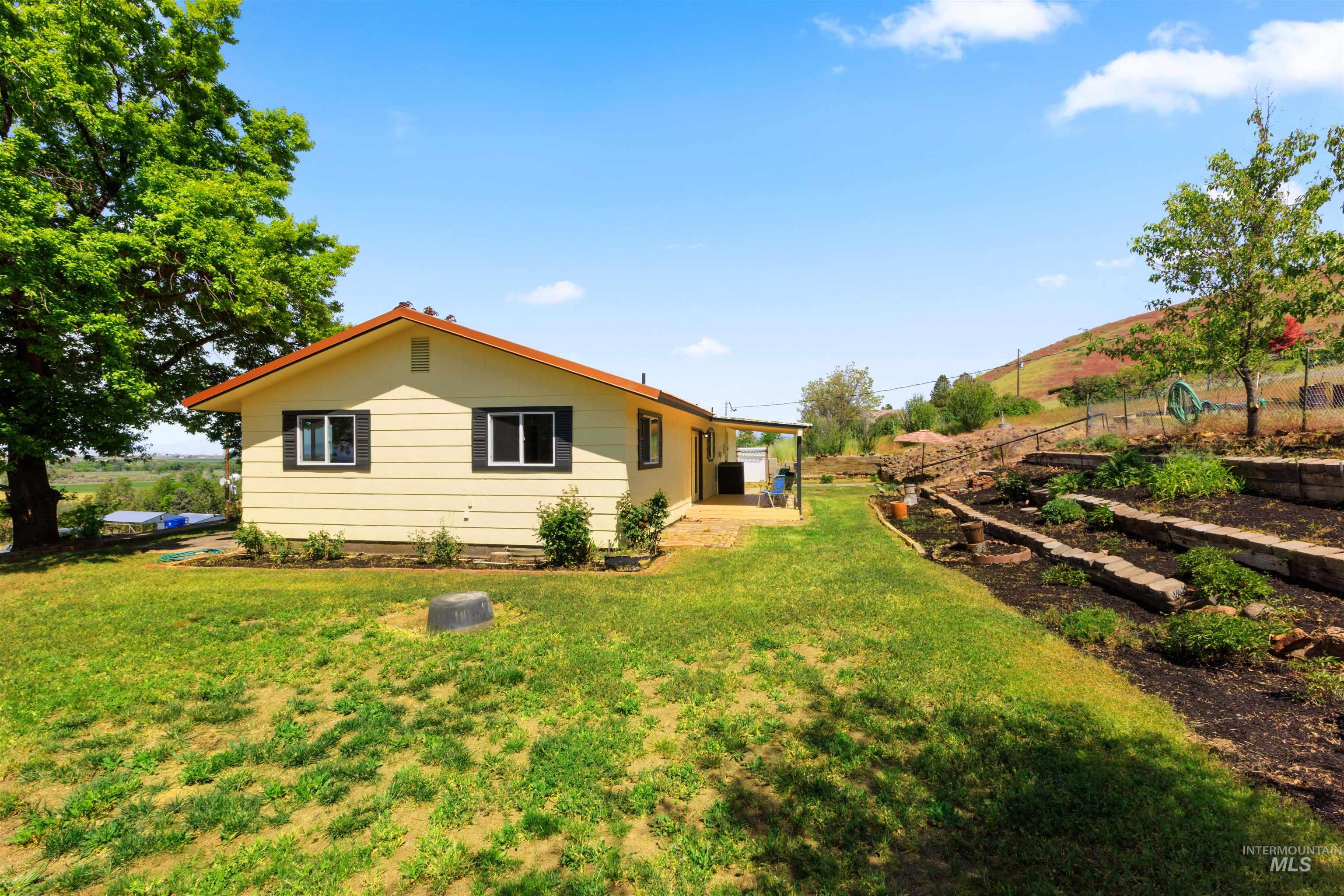12184 Hill Road Payette, ID 83661 - Photo 7 of 35 Rear exterior featuring a covered patio, tiered landscaping, and expansive green space