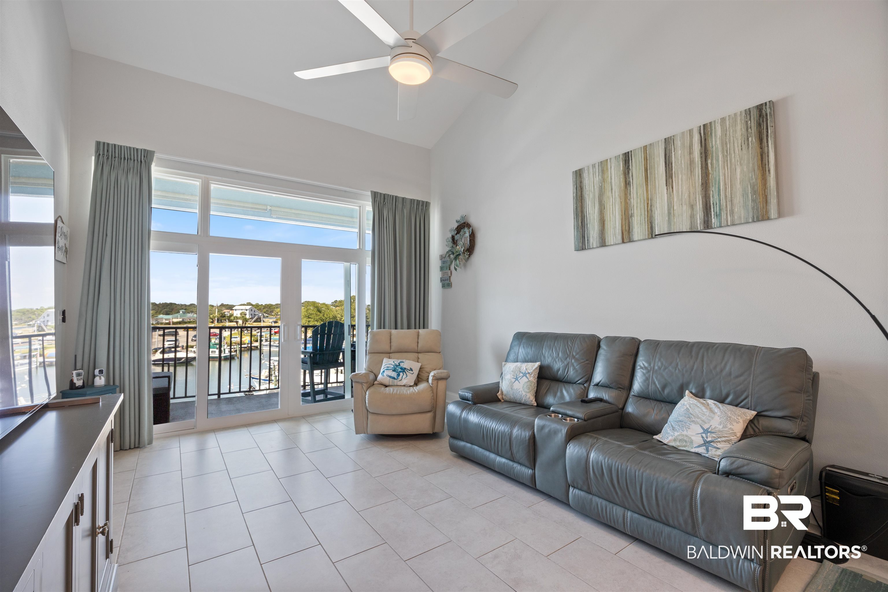Living room featuring light tile patterned flooring, a water view, ceiling fan, and high vaulted ceiling