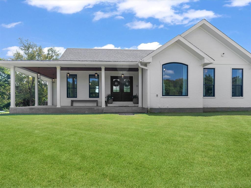 a view of a white house with a big yard and potted plants
