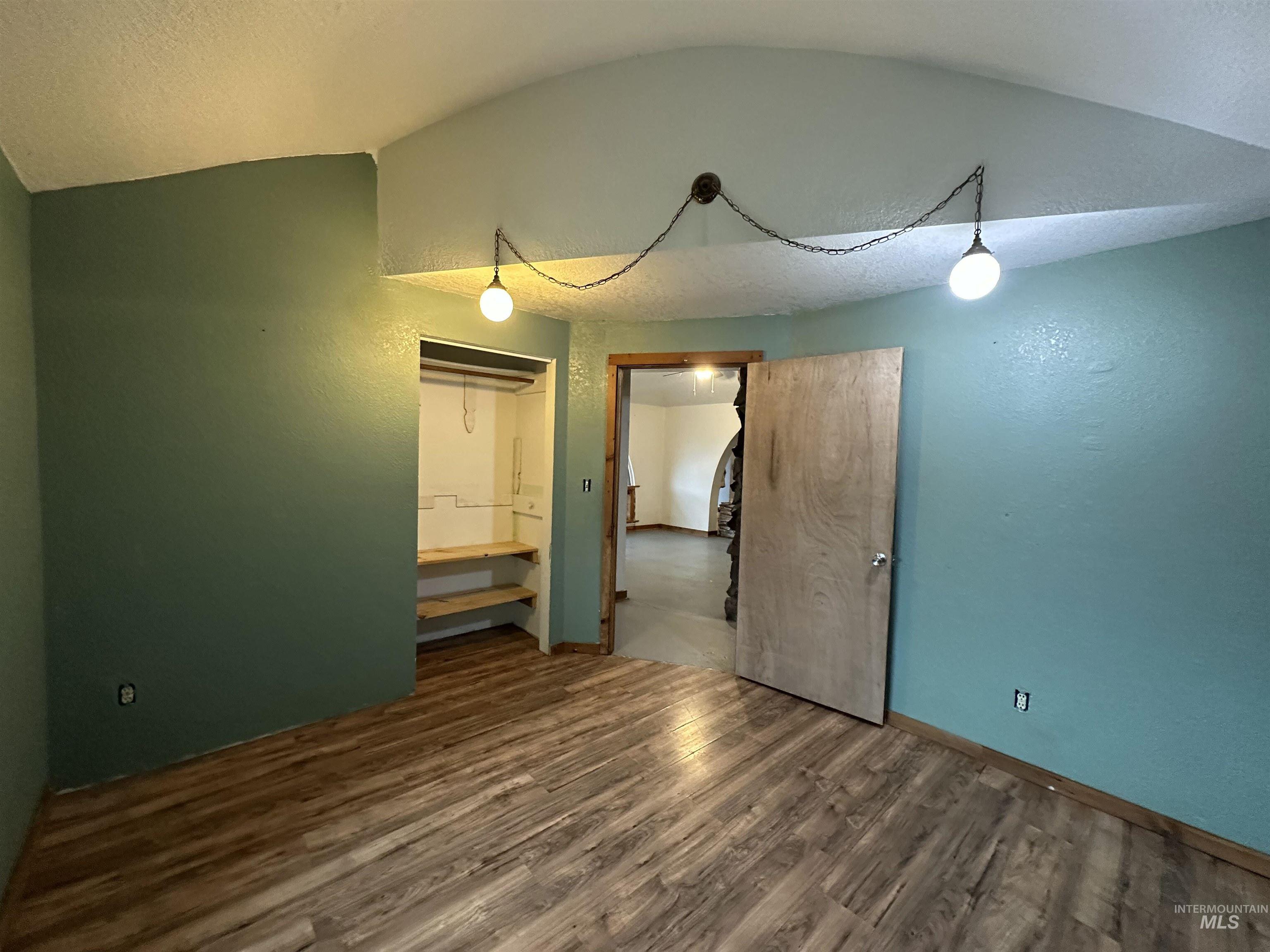 5860 Akron Road New Plymouth, ID 83655 - Photo 19 of 33 Empty room featuring wood finished floors, lofted ceiling, a textured wall, and a textured ceiling